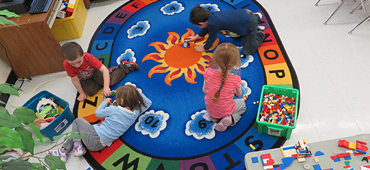 Children play with Lego on a colourful alphabet rug.