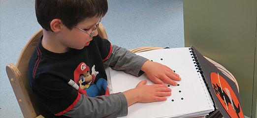 A boy who is visually impaired reads a book with raised dots, a precursor to learning to read in Braille.