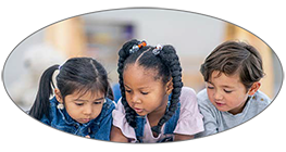 A group of three multi-ethnic preschool children lay on the floor intensely reading together