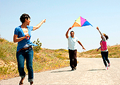 A mother and father are having fun flying a kite with their young adolescent daughter.